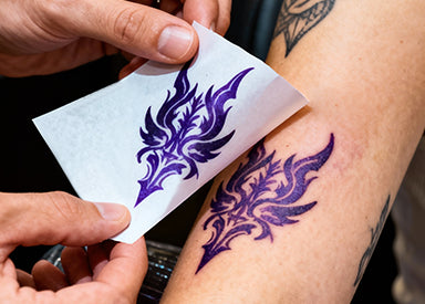 Purple tattoo design being applied to a person's arm with a stencil.